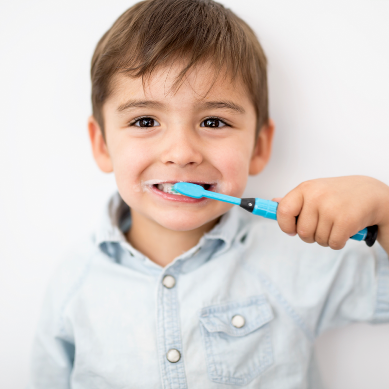An image of a toddler in a button-up shit brushing their teeth with a bright blue toothbrush.